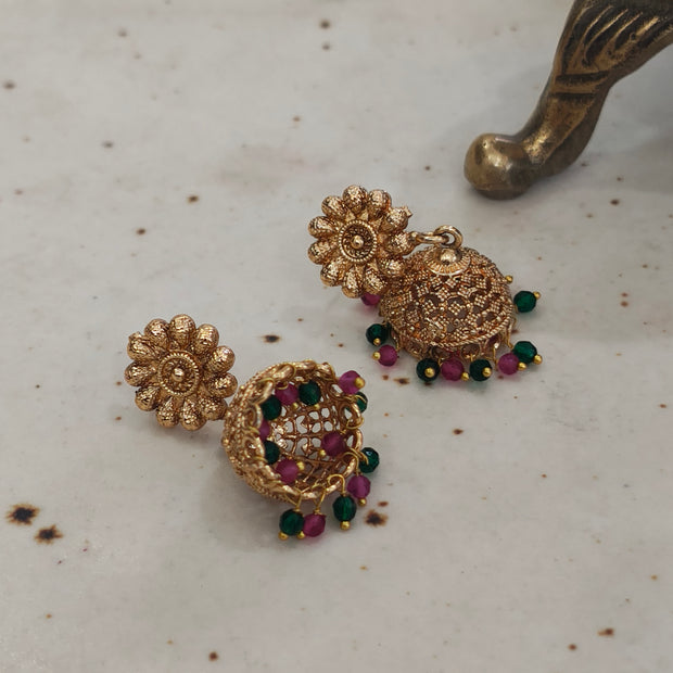 Gold plated jhumki earrings with pink and green pearl drops showcased on a marble surface.