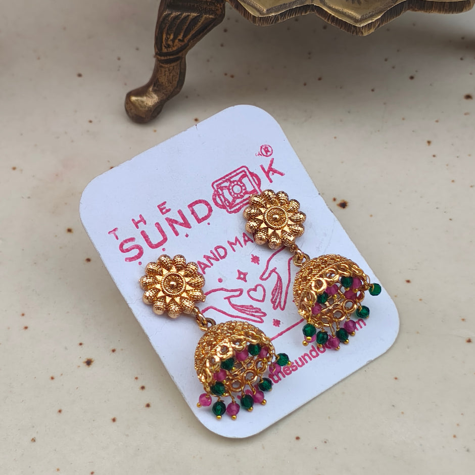 Gold plated jhumki earrings with pink and green pearl drops showcasing intricate design and vibrant colors.