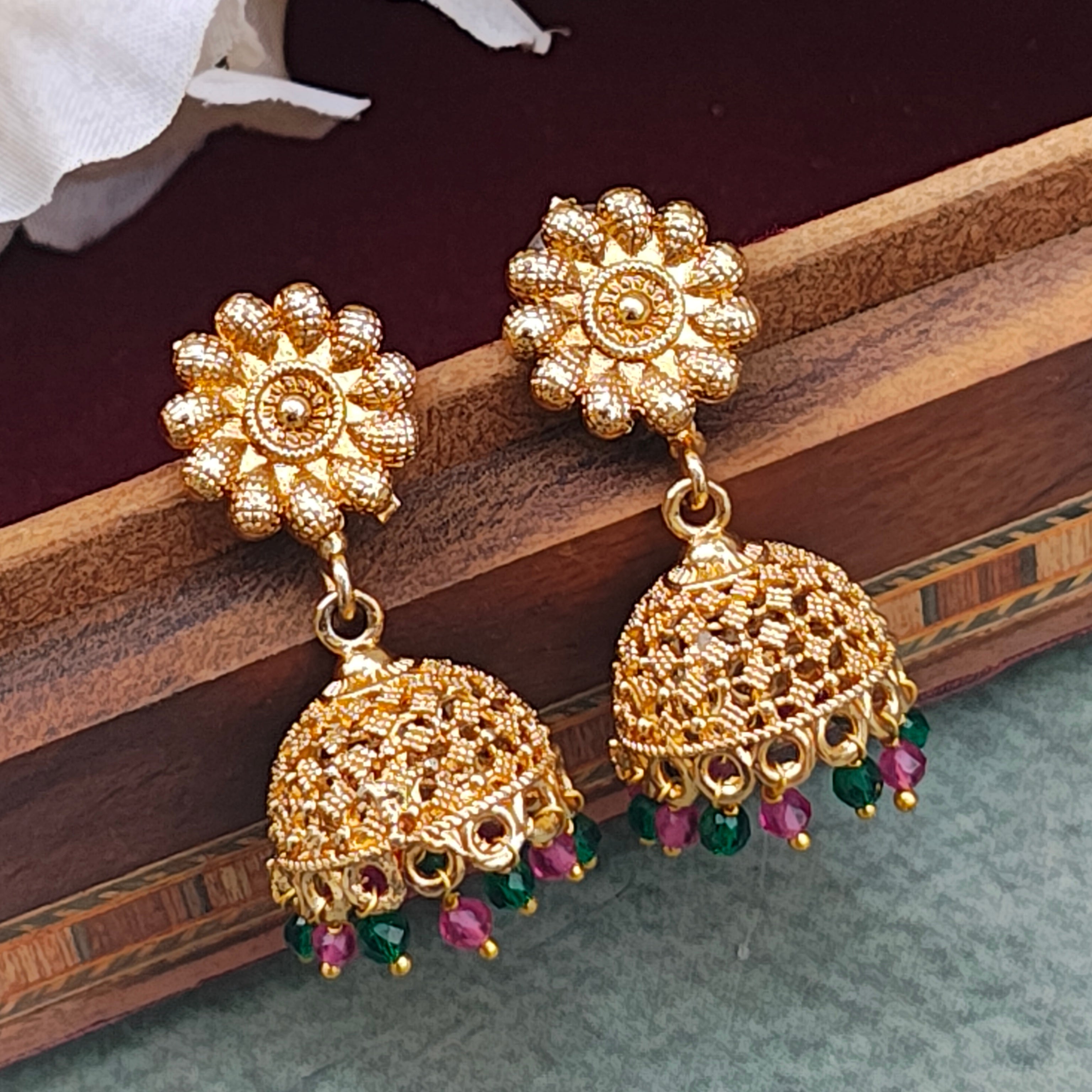 gold plated jhumki earrings with pink and green pearl drops showcased on a wooden box.