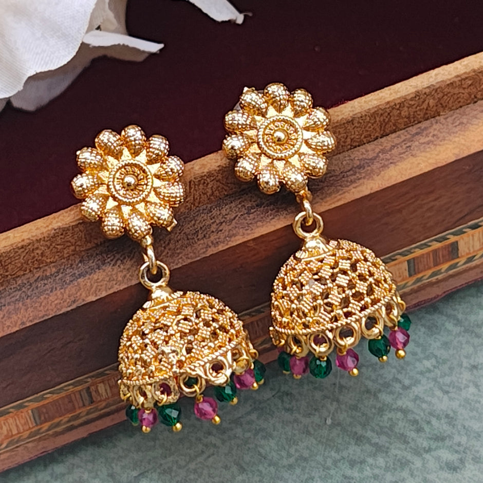 gold plated jhumki earrings with pink and green pearl drops showcased on a wooden box.